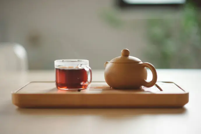 Clear glass cup with tea near a brown ceramic teapot